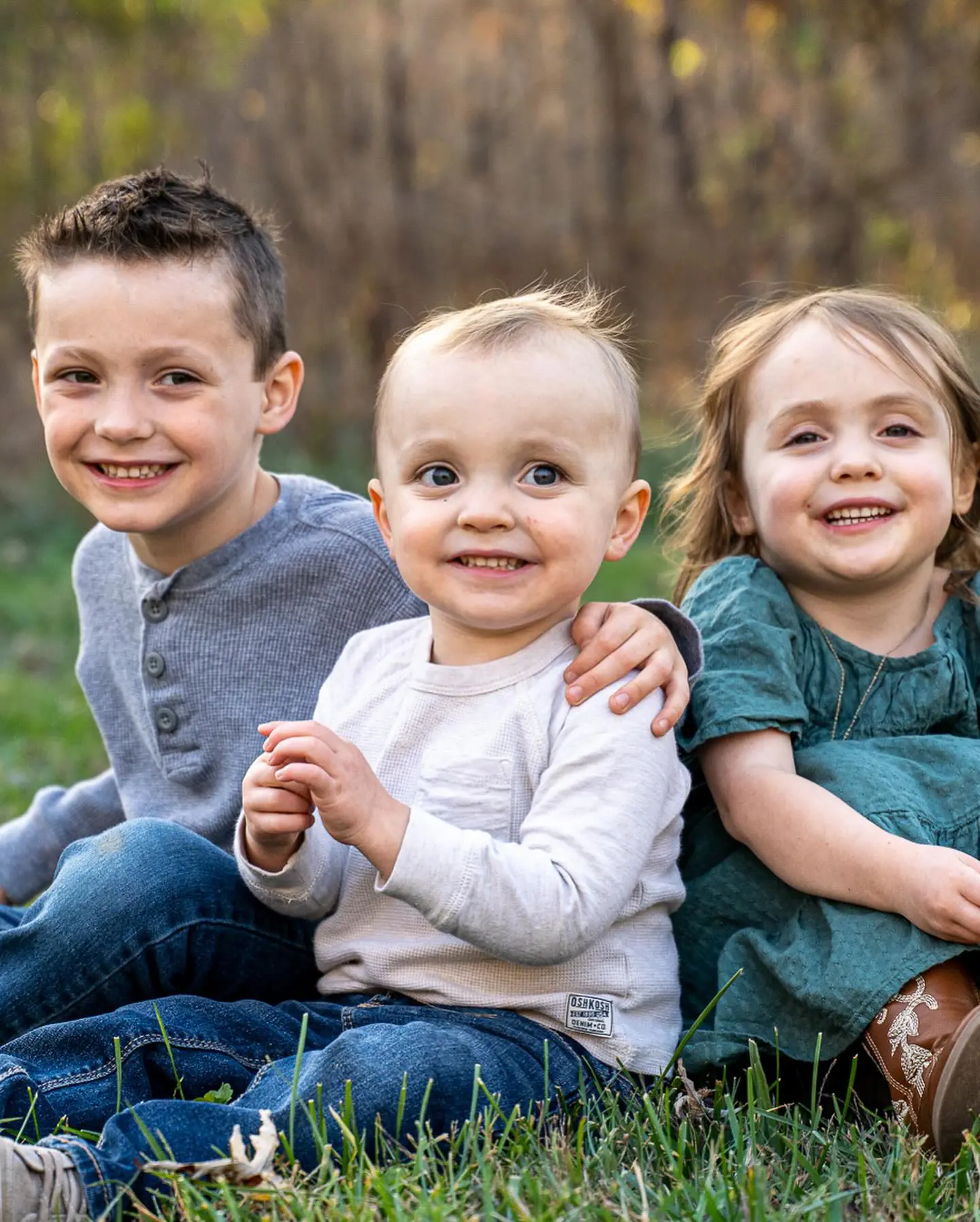 Three young siblings sitting together outdoors